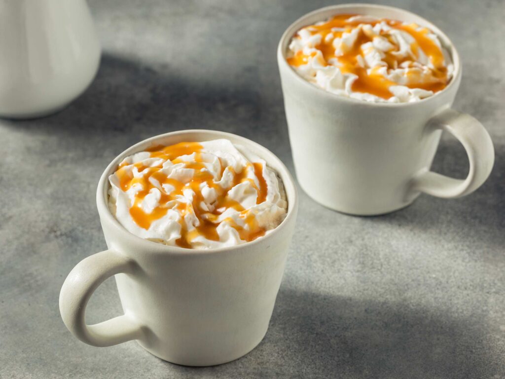 2 mugs of salted caramel hot cocoa with whipped cream and caramel drizzles