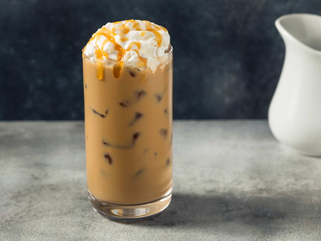A glass of iced salted caramel cocoa topped with whipped creak and caramel drizzles