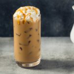 A glass of iced salted caramel cocoa topped with whipped creak and caramel drizzles