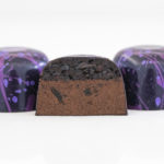 3 raspberry fig truffles in deep purple with light purple and pink splatters with center truffle halved to show chocolate ganache and a dollop of raspberry fig preserves