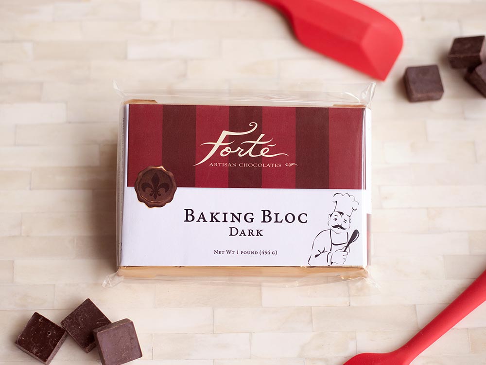 Packaged block of dark chocolate with two red spatulas and 6 small scattered cubes of chocolate