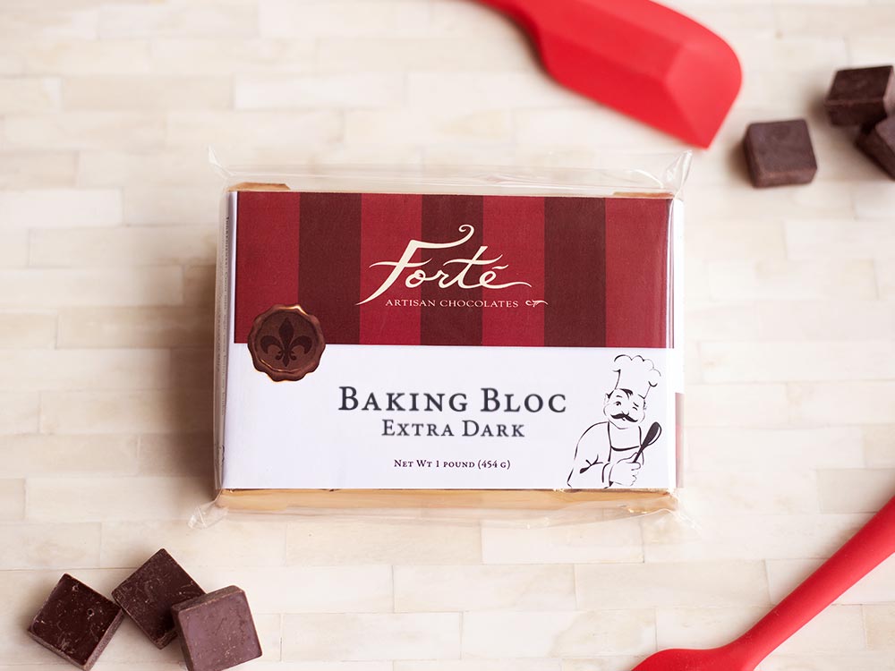 Packaged block of extra dark chocolate with two red spatulas and 6 scattered small cubes of dark chocolate