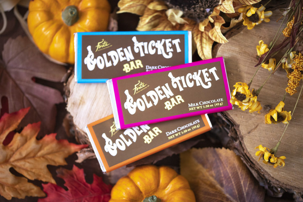 3 Golden Ticket bars of different flavors set on fall decor of leaves pumpkin and dried flowers