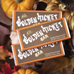 3 dark chocolate golden ticket bars with orange borders atop dried fall leaves