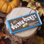 Dark chocolate and sea salt golden ticket bar with blue border atop scattered fall leaves