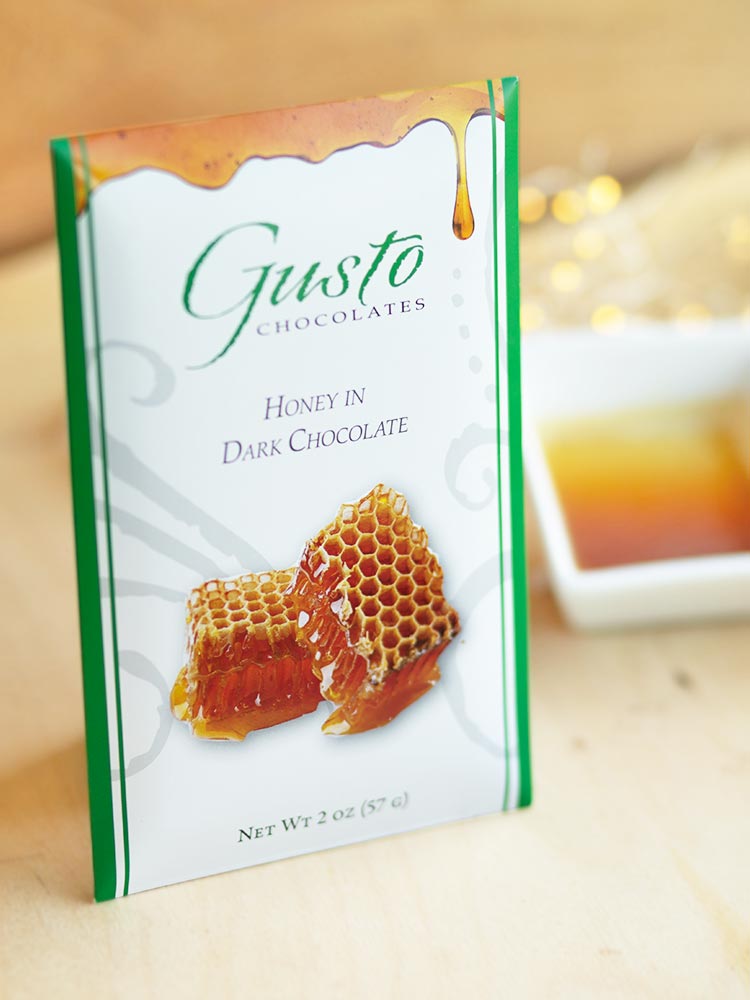 Green-edged honey in dark chocolate bar package with ramekin of honey on the side