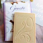 Unwrapped balsamic vinegar in white chocolate bar atop the purple lined packaging sitting on a happy wedding day card with white flowers