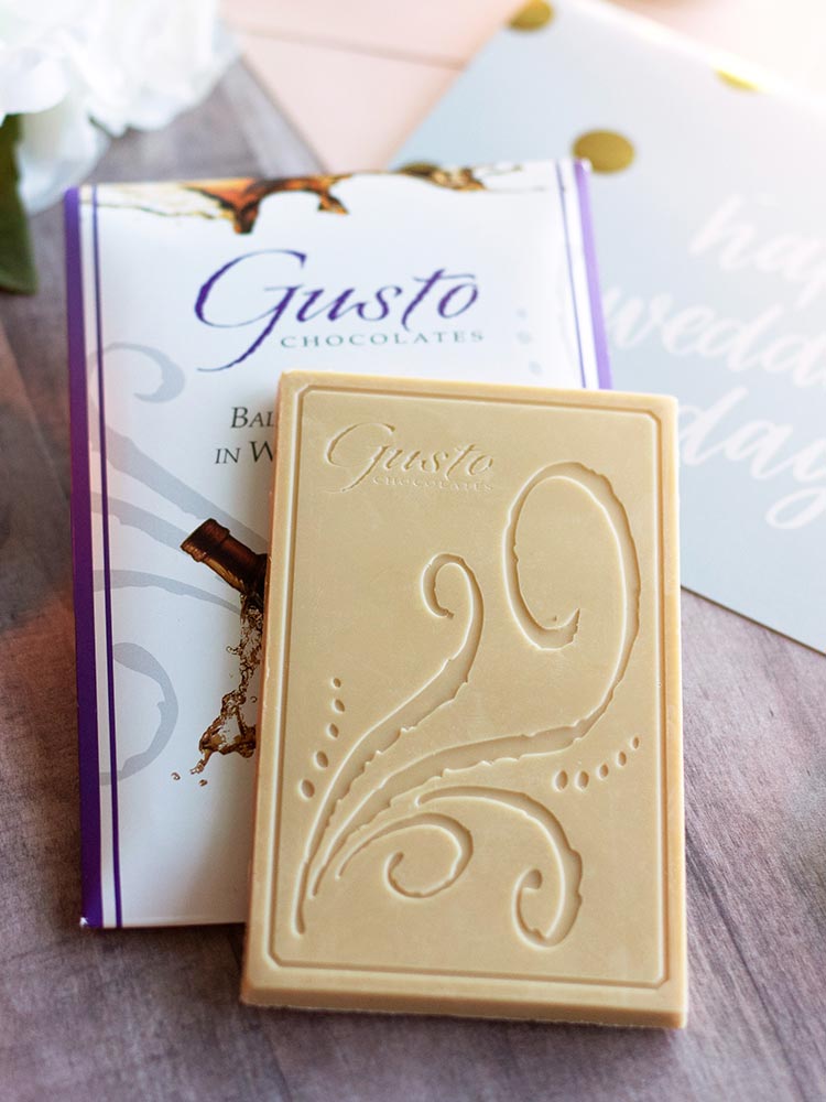 Unwrapped balsamic vinegar in white chocolate bar atop the purple lined packaging sitting on a happy wedding day card with white flowers