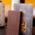 Fortunato chocolate bar with logo and chocolate mold design standing in front of fortunate packaging showing cacao pods with bottles of wine in background