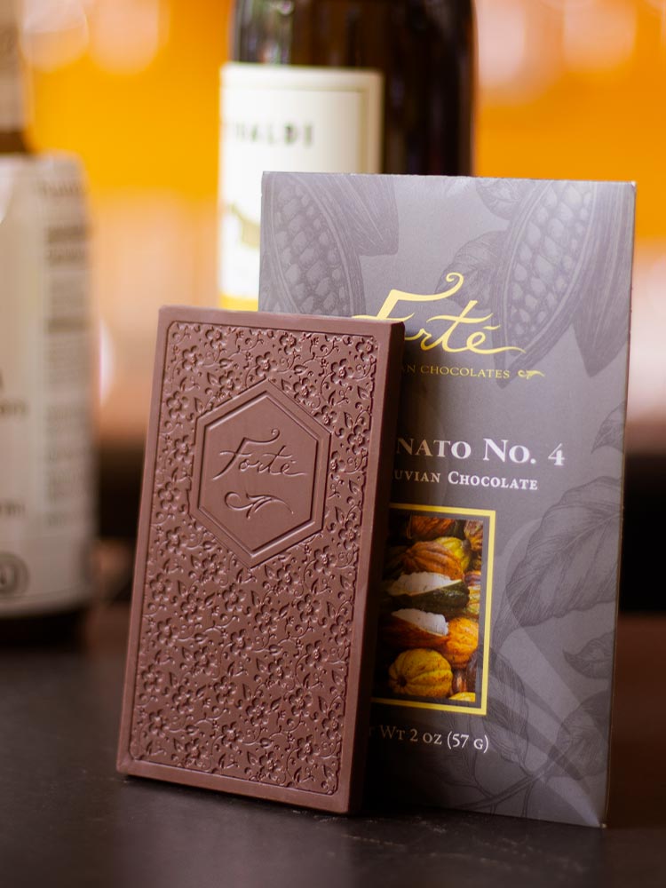 Fortunato chocolate bar with logo and chocolate mold design standing in front of fortunate packaging showing cacao pods with bottles of wine in background