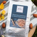 Marcona Almond bar sitting on black and white chefs towel with whole almonds and yellow flowers