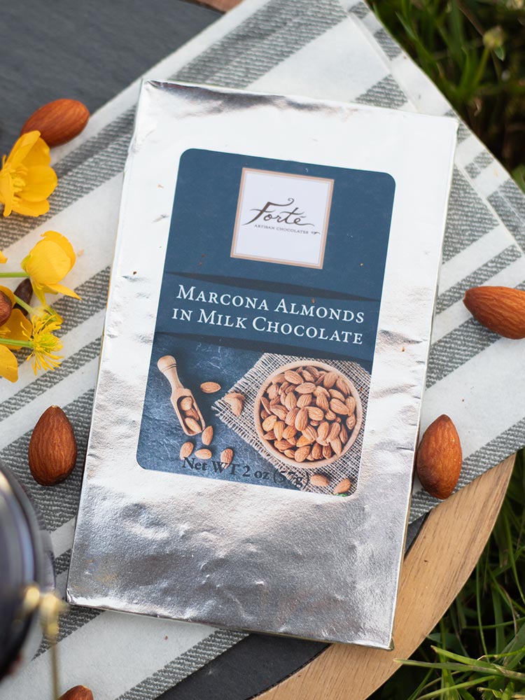 Marcona Almond bar sitting on black and white chefs towel with whole almonds and yellow flowers
