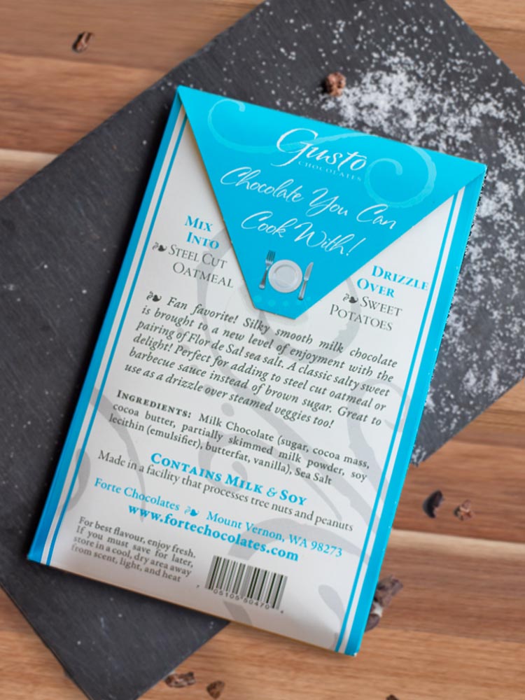 Back of milk sea salt packaging on top of slate cutting board sprinkled with sea salt and chocolate shavings