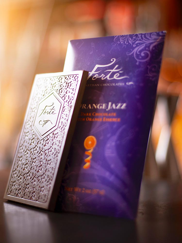 Dramatically lit chocolate bar spotlighting Forte logo and bar mold design in front of Orange Jazz chocolate bar packaging in purple