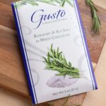 Gusto rosemary and sea salt in white chocolate packaging on a cutting board dusted with sea salt and sprigs of rosemary