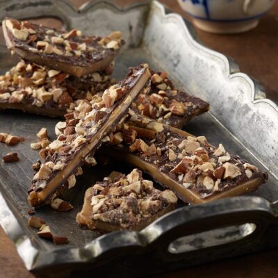 Almond toffee butter crunch on a silver tray with blue and white mug in background