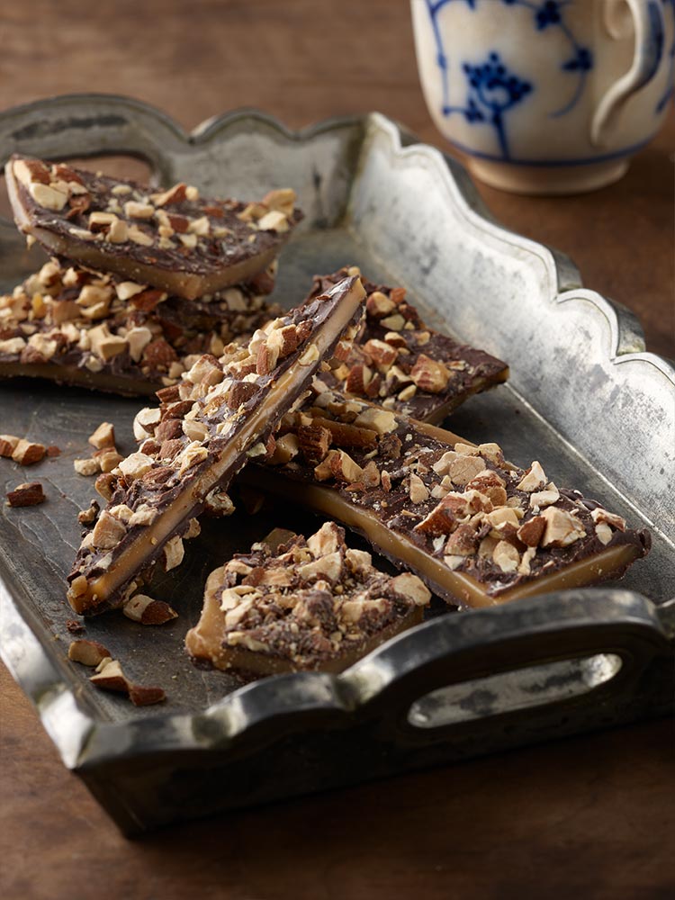 Almond toffee butter crunch on a silver tray with blue and white mug in background
