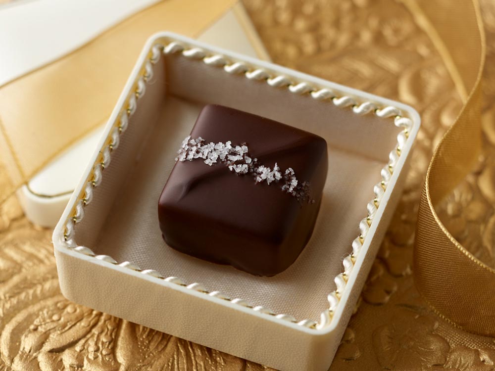 Single sea salt dark chocolate caramel in a jewel box on a gold background