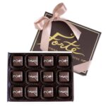 12 pieces of sea salt dark caramels in an open box with lid behind including a satin pink ribbon tied in a bow
