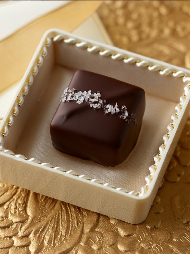 Single sea salt dark chocolate caramel in a jewel box on a gold background