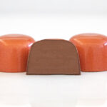 3 orange-brown classic milk chocolate truffles with middle one sliced in half showing milk chocolate ganache
