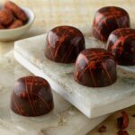 Five classic dark chocolate truffles arranged on two marble slabs with cacao beans