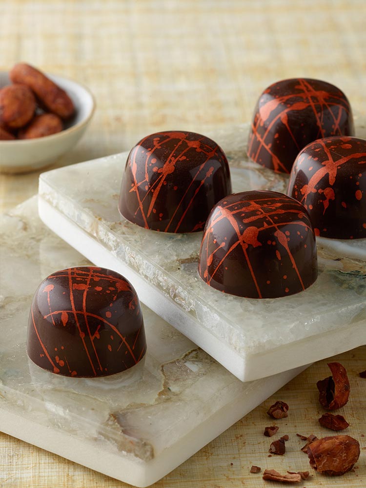 Five classic dark chocolate truffles arranged on two marble slabs with cacao beans