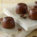 Four espresso truffles with coffee beans artfully arranged on two marble slabs
