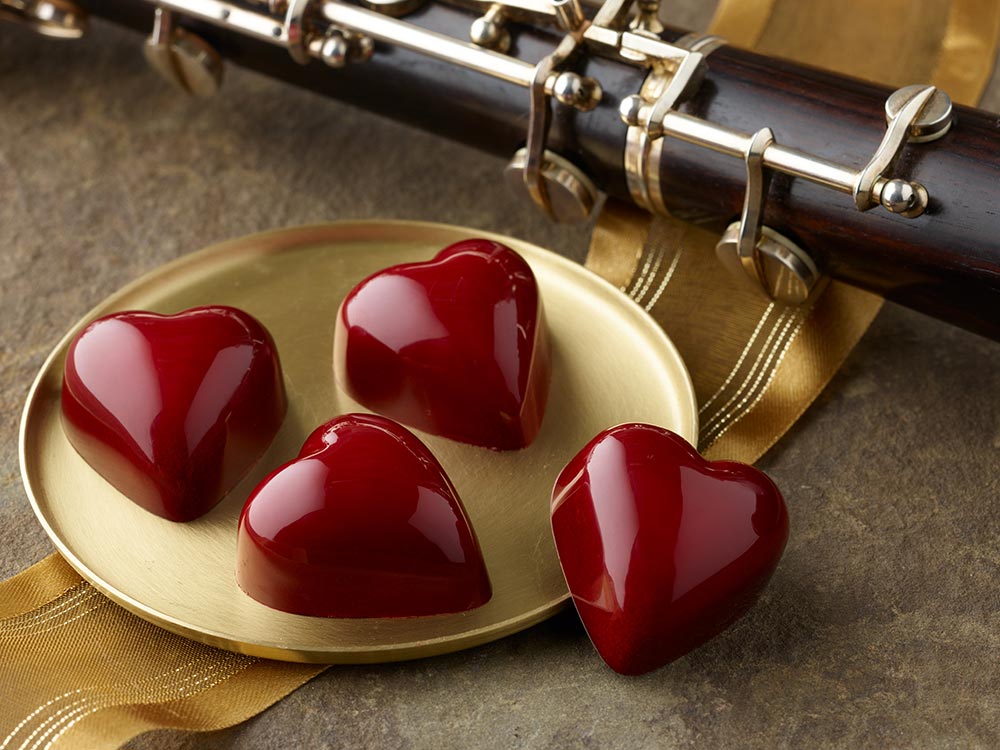 4 shinny red heart truffles on gold plate with oboe in background.