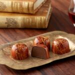 4 peanut butter truffles with one sliced in half showing peanut buttery ganache inside the brown and gold splattered cup placed on a brass oblong plate in front of two antique books