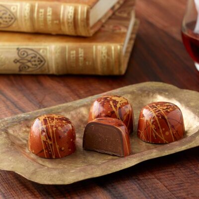 4 peanut butter truffles with one sliced in half showing peanut buttery ganache inside the brown and gold splattered cup placed on a brass oblong plate in front of two antique books