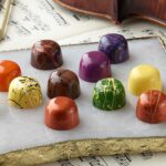 12 assorted chocolate truffles artfully arranged on a white marble slab on top of violin music and violin with bow