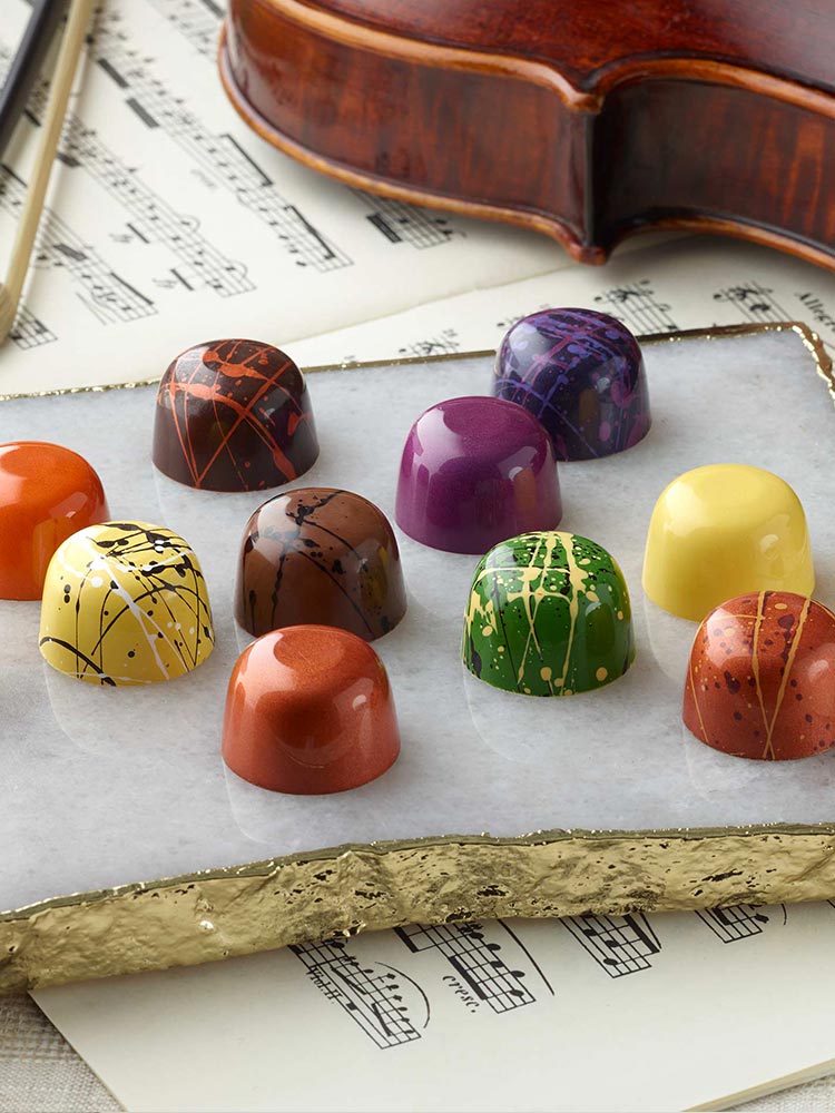 12 assorted chocolate truffles artfully arranged on a white marble slab on top of violin music and violin with bow