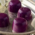 Close up 5 dark purple vegan superfood truffles arranged on a silver tray with a white orchid
