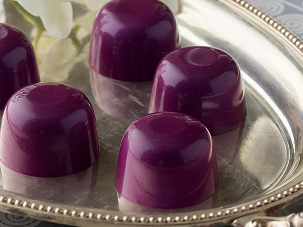 Close up 5 dark purple vegan superfood truffles arranged on a silver tray with a white orchid