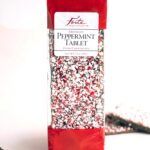 Bag of dark chocolate peppermint bark with red edges and a peppermint stick in foreground