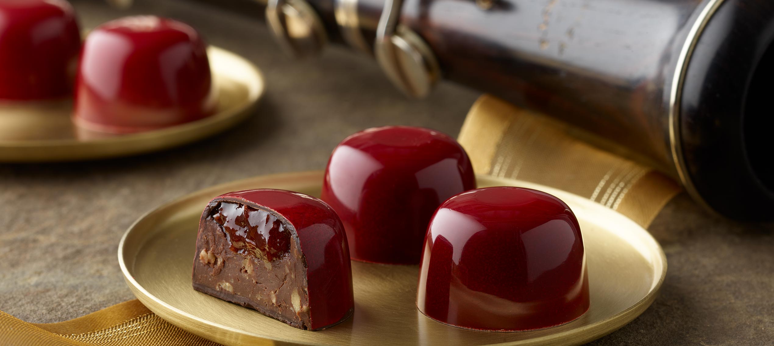 Bright red truffles on two small gold plates with one cut in half showing cherry almond ganache with oboe bell in background