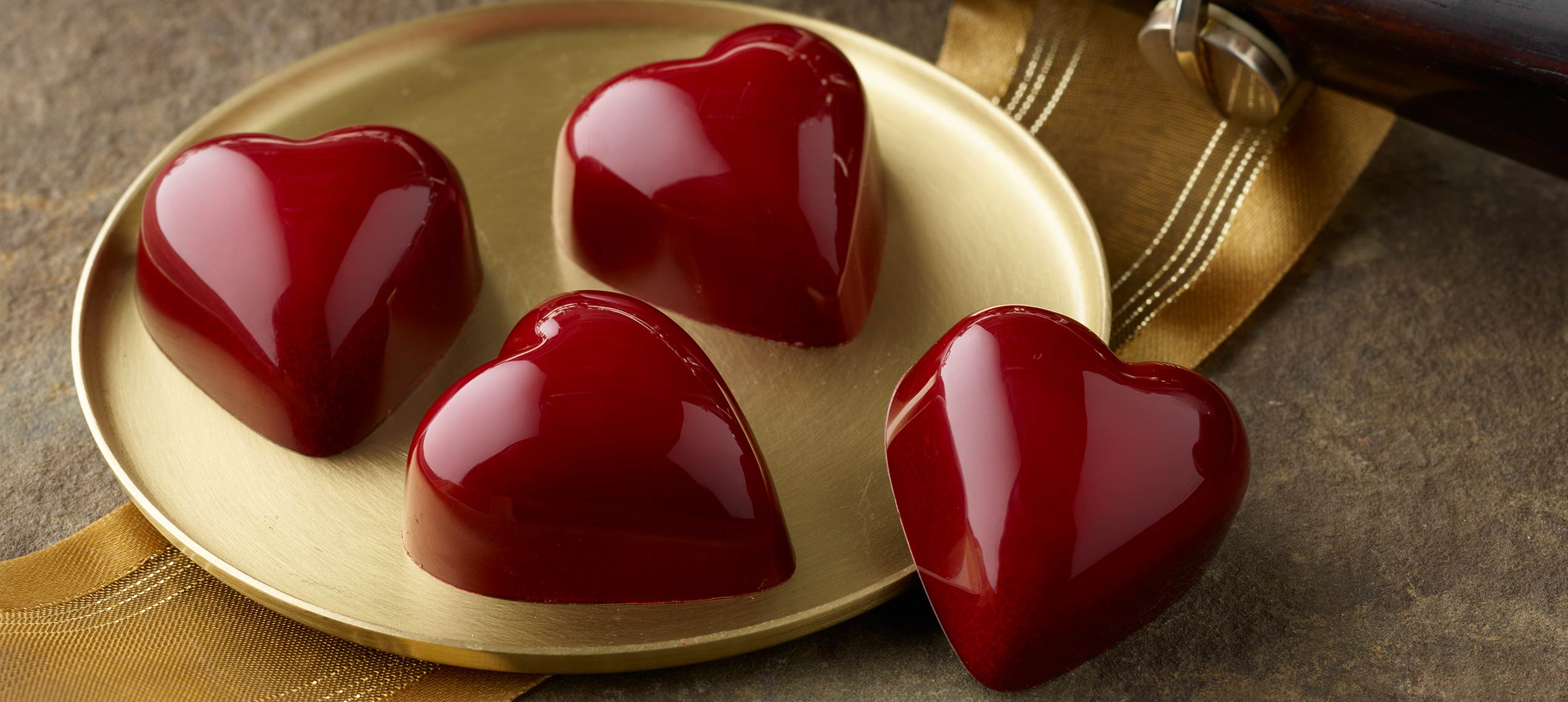 Four red heart truffles on a gold platter on top of a wide gold ribbon