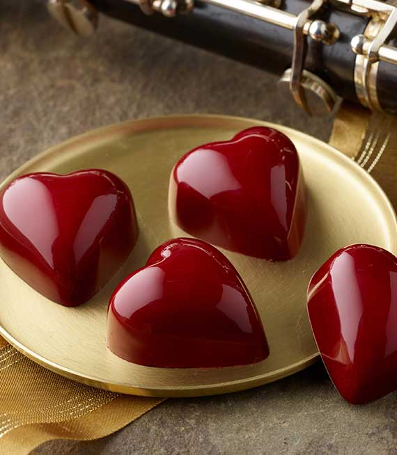 Four red heart shaped truffles on a gold platter with part of an oboe in background