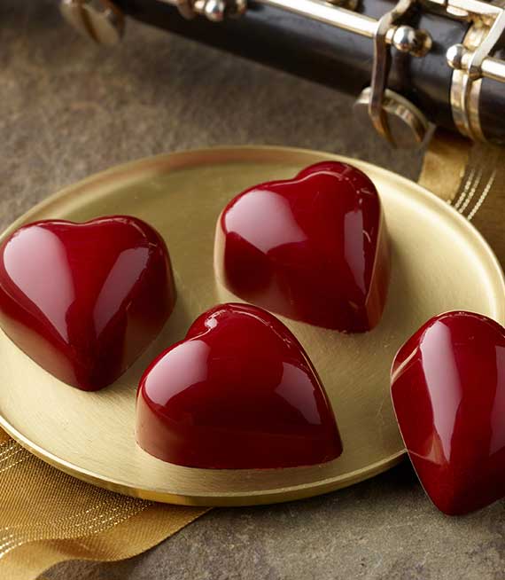 Four bright red heart truffles on a small gold plate with oboe keys and gold ribbon