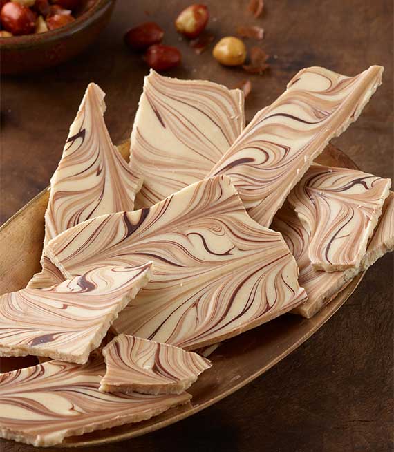 Oblong gold bowl containing slabs of Tiger Bark in brown and white swirls with peanuts scattered in background