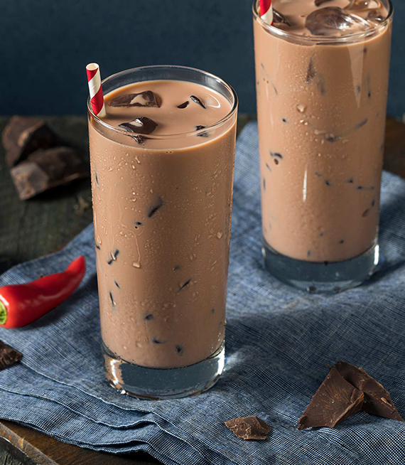 2 Aztec Iced Cocoa in a tall glass with a red chili pepper and a blue tablecloth